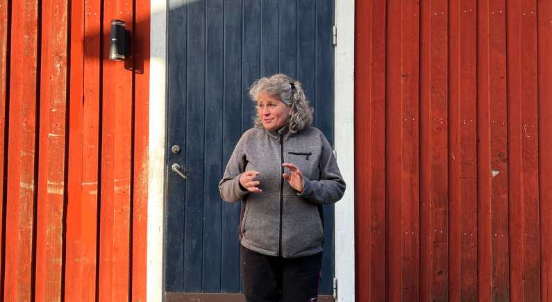 Kvinna framför dörr på röd stuga