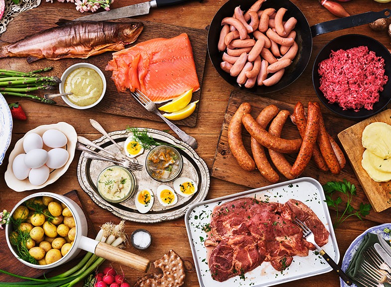 Midsommarmat på ett bord. Rökt och gravad fisk, sill, korvar, potatis och fläskkarré