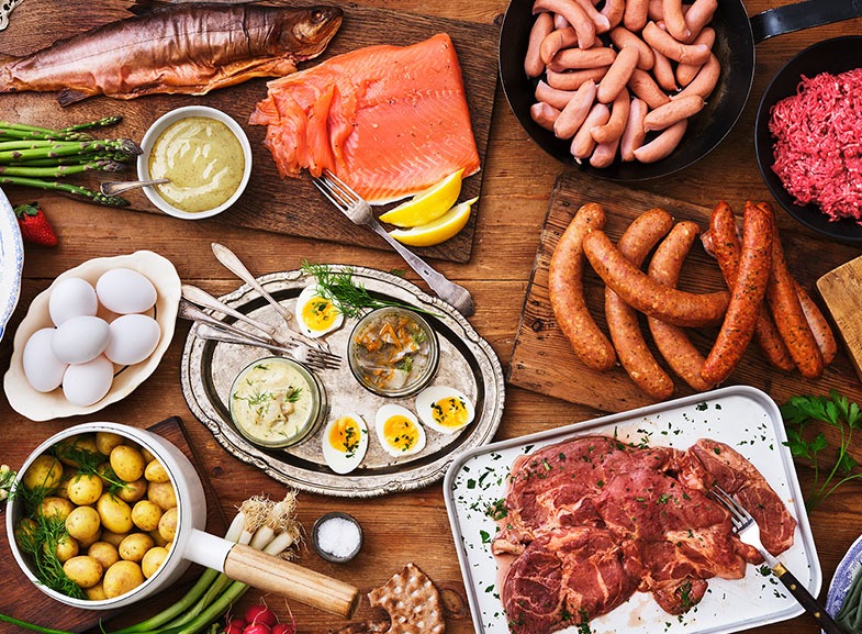 Midsommarmat på ett bord. Rökt och gravad fisk, sill, korvar, potatis och fläskkarré